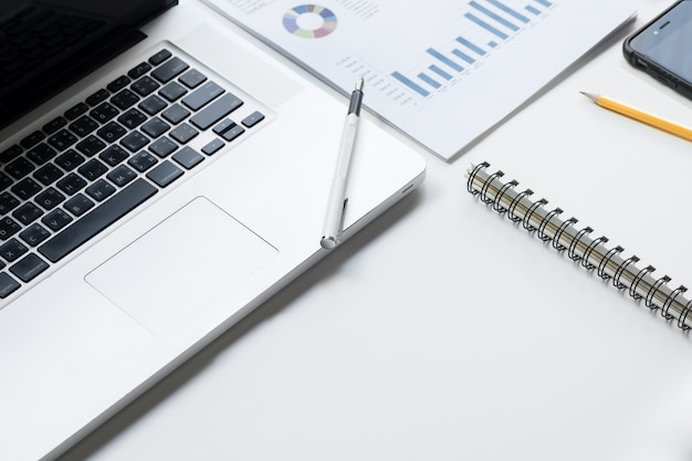 Business desk with a keyboard, report graph chart, pen and tablet on white table.