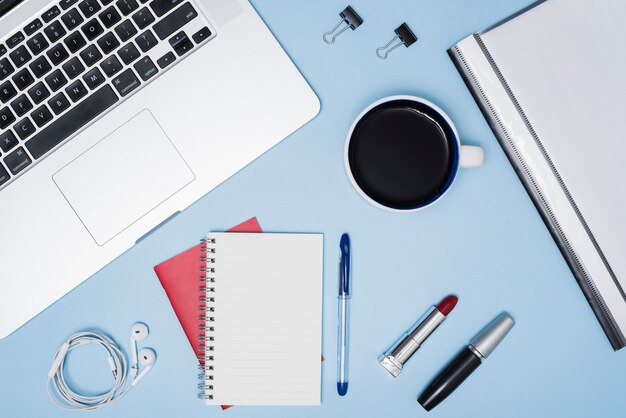 Business desk with make-up objects; coffee cup; files and earphone over blue background