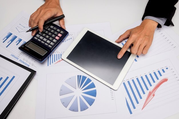 business documents on office table with smart phone and digital tablet and man working in the background.