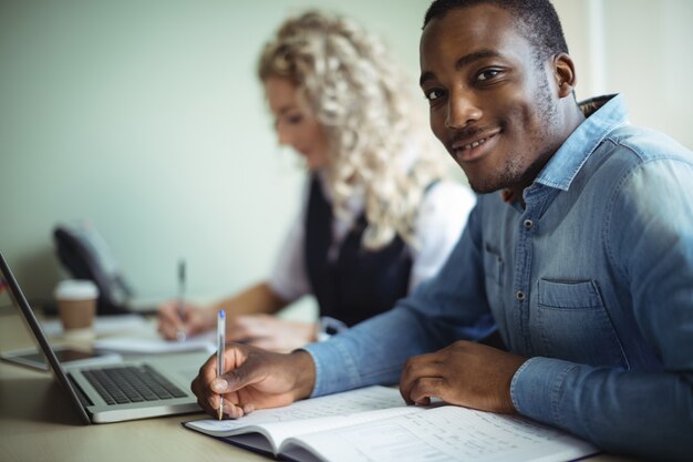 Business executive taking notes while using laptop