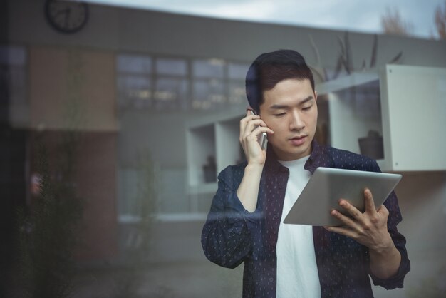 Business executive talking on mobile phone while using digital tablet