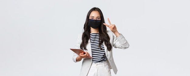 Business finance and employment covid19 preventing virus and social distancing concept Cheerful young asian office worker female entrepreneur with digital tablet in protective mask