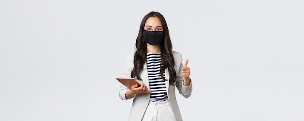 Business finance and employment covid19 preventing virus and social distancing concept Smiling real estate broker wearing protective mask during meeting pointing camera hold digital tablet