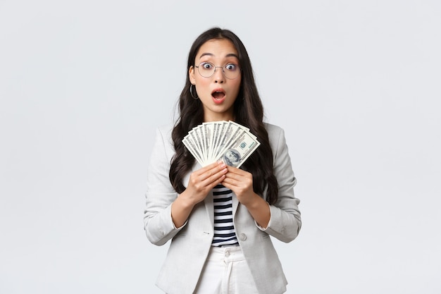 Free photo business, finance and employment, entrepreneur and money concept. amazed and speechless young asian businesswoman earn first paycheck for selling house, holdin cash and stare astonished.