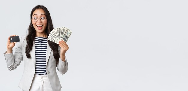 비즈니스 금융 및 고용 기업가 및 돈 개념 신용카드 흰색 배경에 흥분하여 예금에 현금을 넣는 것에 대해 생각하는 우유부단한 귀여운 아시아 사무실 여성