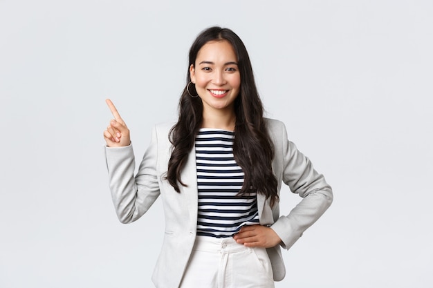 Free Photo business, finance and employment, female successful entrepreneurs concept. cheerful successful businesswoman in white suit pointing fingers upper left corner, showing advertisement