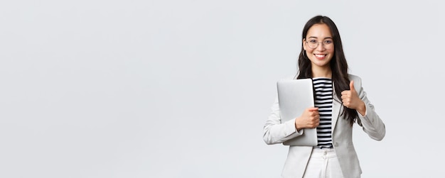 Free photo business finance and employment female successful entrepreneurs concept confident goodlooking therapist or businesswoman in white suit holding laptop and showing thumbsup