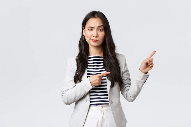 Business, finance and employment, female successful entrepreneurs concept. Skeptical and hesitant young asian businesswoman dont trust this promo, smirk doubtful and pointing upper right corner