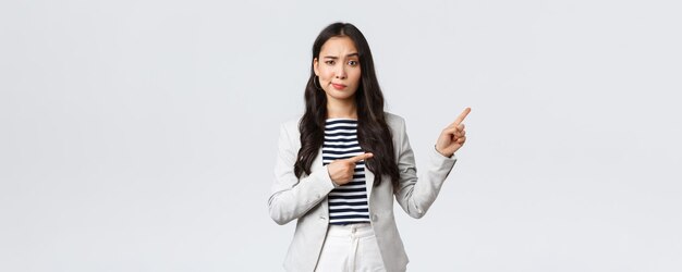 Business finance and employment female successful entrepreneurs concept Skeptical and hesitant young asian businesswoman dont trust this promo smirk doubtful and pointing upper right corner