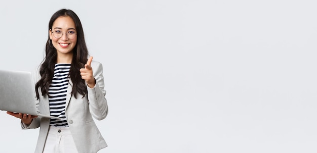Free Photo business finance and employment female successful entrepreneurs concept smiling pleased businesswoman praise coworker who made good point pointing finger camera satisfied hold laptop
