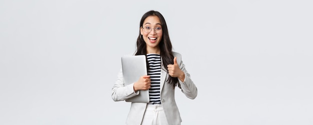 Business finance and employment female successful entrepreneurs concept Young confident businesswoman in glasses showing thumbsup gesture hold laptop guarantee best service quality