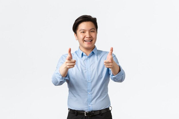 Business, finance and people concept. Satisfied asian businessman with teeth braces showing thumbs-up, office worker recommend product or compliment good work, white background