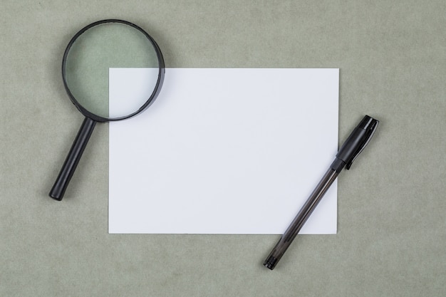 Business and financial concept with magnifying glass, pen, blank paper on grey background flat lay.