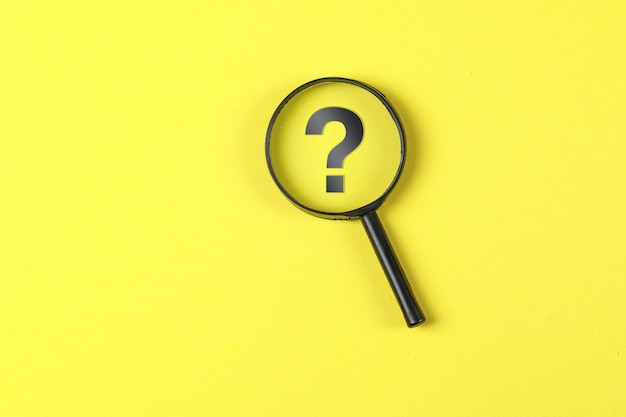 Business and financial concept with magnifying glass, question mark on yellow background flat lay.