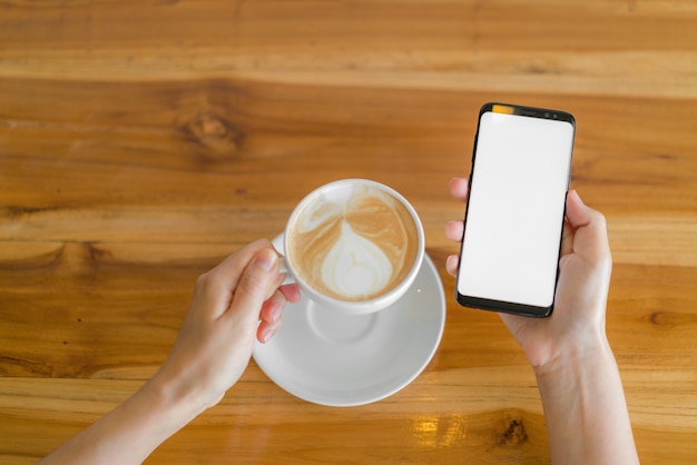 Mano d'affari con il telefono cellulare e il latte art coffee.