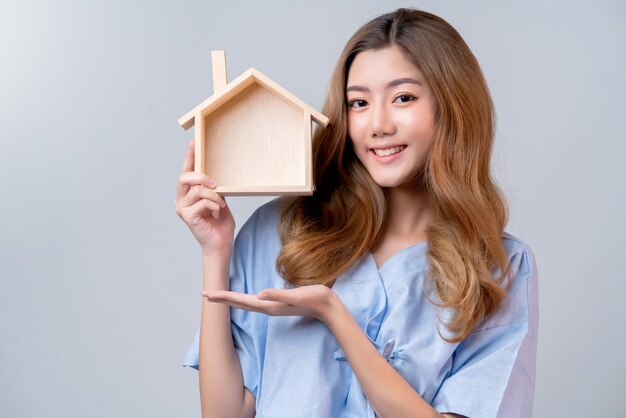 Business healthy insurance beautiful asian female in hospital uniform smile with hand house model ideas for happy insurance package and promotion with hospital blur background