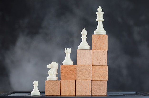 Business hierarchy concept with figures on pyramid of wooden blocks on foggy and chessboard side view.