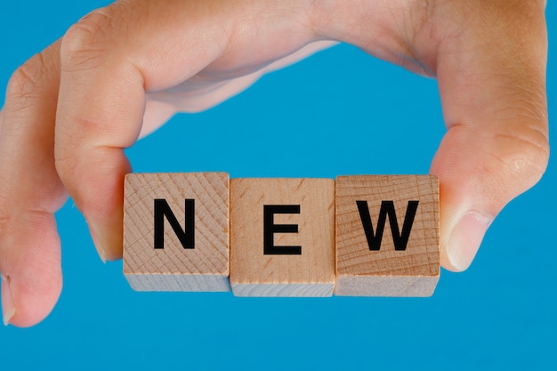 Business idea concept on blue table side view. hand holding wooden cubes with word new.