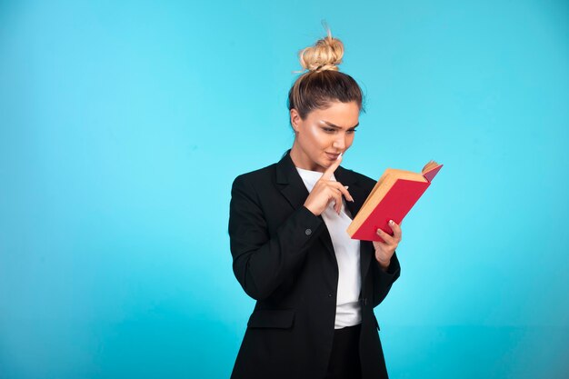 Business lady in black blazer with a red book and reading it. 