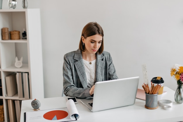 Business lady in gray jacket working in laptop. Portrait of woman in office.