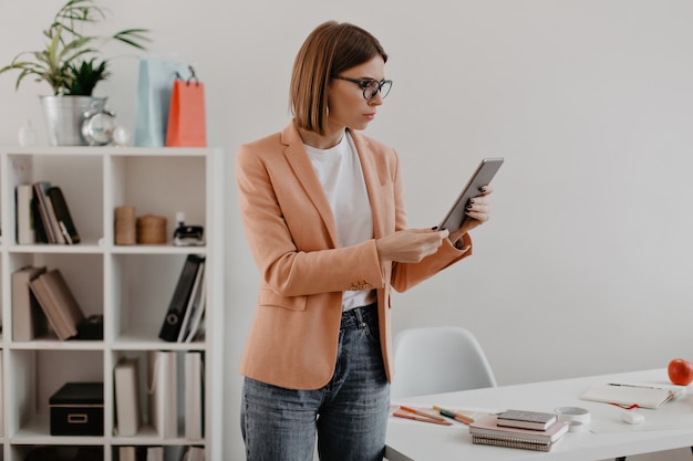 ビジネスの女性はタブレットに戸惑っているように見えます。オフィスでポーズをとる薄着の若い女性。