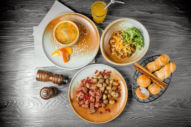 ビジネスランチ赤身の肉のグリルローストポテト野菜スープキノコサラダパン飲み物とテーブルの上の黒胡椒
