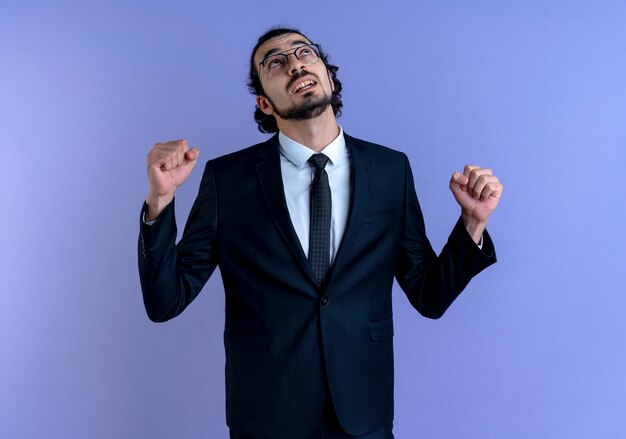 Business man in black suit and glasses looking up clenching fist