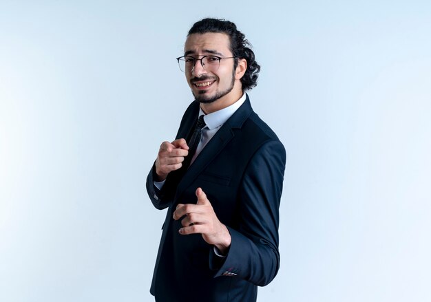 검은 양복과 흰 벽 위에 유쾌하게 서있는 전면에 검지 손가락으로 가리키는 안경 비즈니스 남자