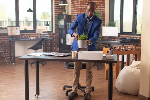 Business man packing up office things in box after getting fired from work. Discharged person being dismissed from job and gathering belongings to leave startup company workplace.