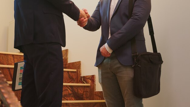 Business man partners executives shaking hands on stairs of office building while talking. Group of professional successful businesspeople in suit working together in modern financial workplace.