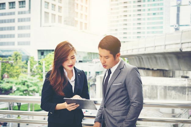 Business man pointing at document with smile and discussing something with her coworker while standing in front of office.