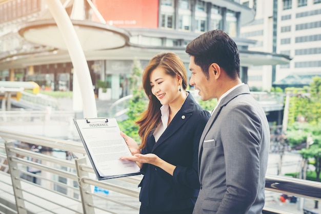 Free photo business man pointing at document with smile and discussing something with her coworker while standing in front of office.