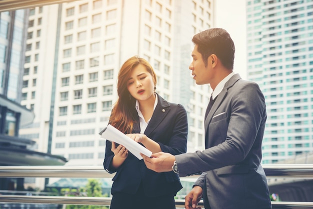 Business man pointing at document with smile and discussing something with her coworker while standing in front of office.