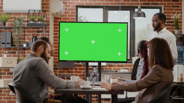 Business man presenting monitor with green screen at meeting with coworkers, looking at mock up background with isolated copy space template. People working with blank chroma key display.