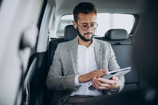 Business man sitting on the back sit of a car using tablet