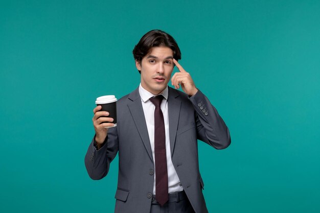 Деловой человек стильный милый красивый мужчина в сером офисном костюме и галстуке думает и держит чашку кофе