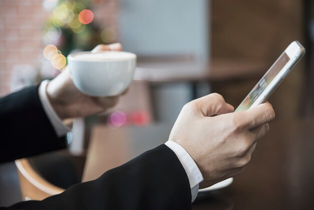 コーヒーショップでコーヒーを飲みながら携帯電話を使用してビジネス男