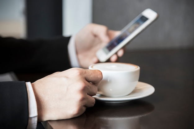 Деловой человек с помощью мобильного телефона, попивая кофе в кафе