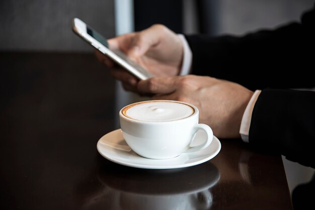 コーヒーショップでコーヒーを飲みながら携帯電話を使用してビジネス男
