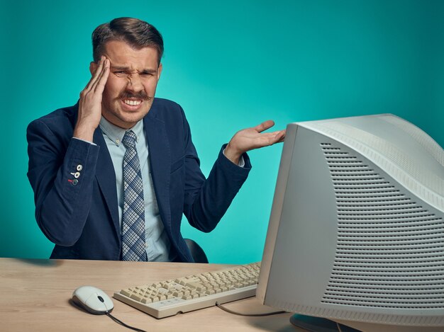 Business man with headache sitting at desk in front of computer