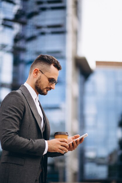 Business man with phone drinking coffee outside skyscraper