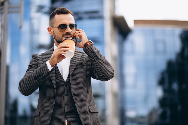 Business man with phone drinking coffee outside skyscraper