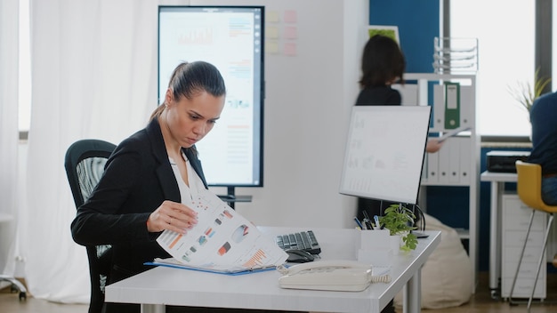 Business manager checking data charts with files and computer for strategy planning and analysis. Engineer working on corporate project with monitor and technology at office desk.