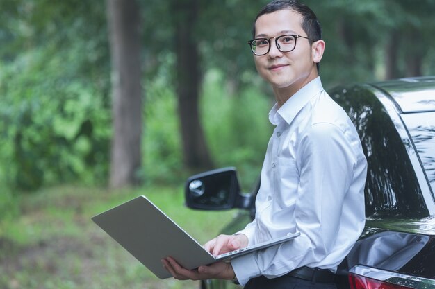 ビジネスマンは、車の側にノートパソコンで動作します。