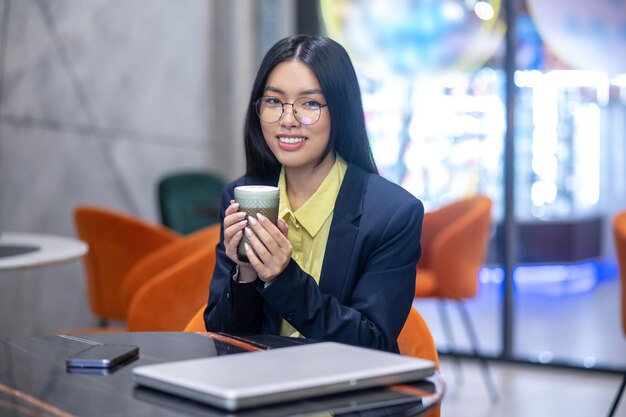 ビジネスの朝。朝のコーヒーを持っているオフィスでアジアのビジネスウーマン