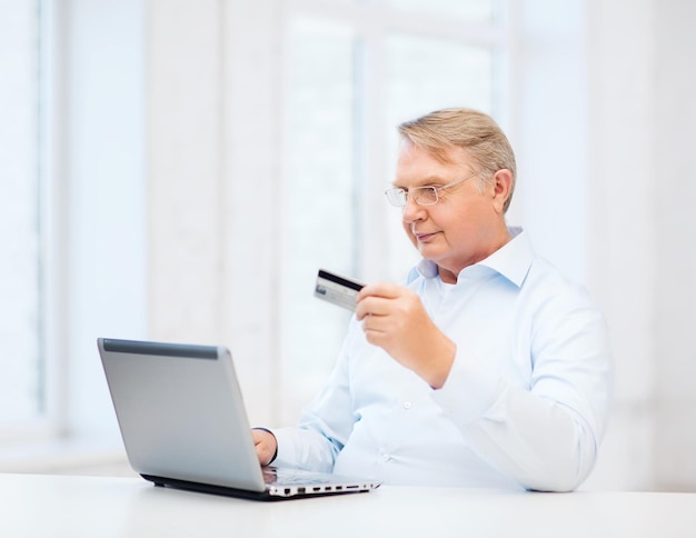 Business, online banking, internet shopping and oldness concept - smiling old man with laptop computer and credit card at home