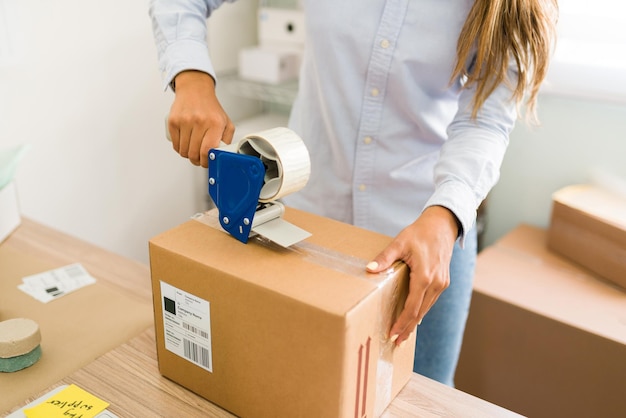 Business owner ready to ship her customers' orders. Close up of female hands putting tape on a big package with products