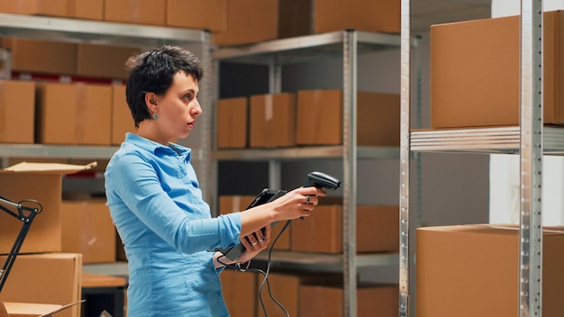 Business owner scanning stock from storehouse shelves, working with scanner to do inventory and check logistics supplies. Female employee using tablet to scan bar code on merchandise. Handheld shot.