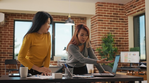 Business partners looking at marketing analysis on laptop, doing research to plan new project application for financial growth. Asian women using sales statistics to work on management