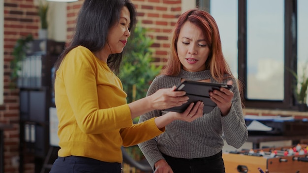 Business partners using tablet and research files in startup office to work on management project. Team of women working together to develop financial strategy and plan success.